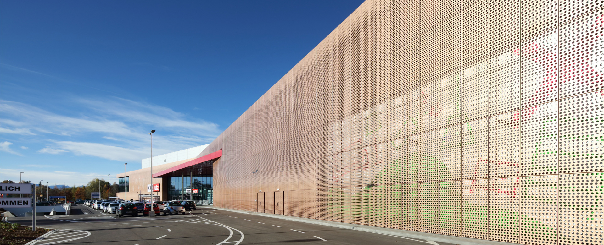 Langgestreckte, perforierte Fassade des Möbelhauses in Duraflon Bright Copper